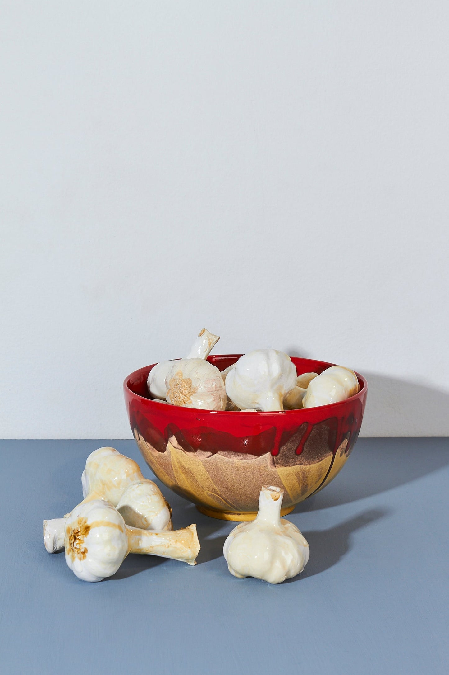 Tazón rojo y dorado de cerámica con ajos decorativos en su interior. Ideal para cocina moderna.