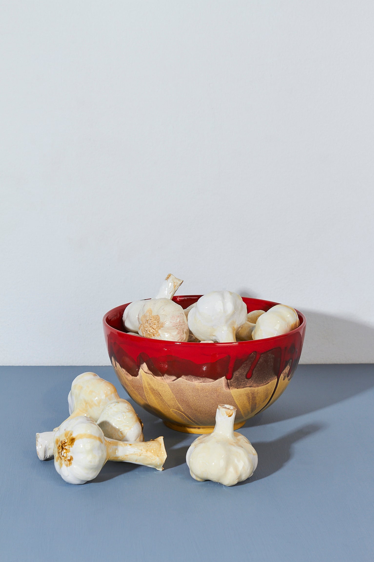 Tazón rojo y dorado de cerámica con ajos decorativos en su interior. Ideal para cocina moderna.