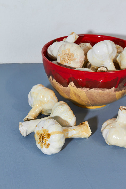 Ajo blanco en tazón de cerámica roja brillante, fondo azul claro, estilo moderno y artesanal.