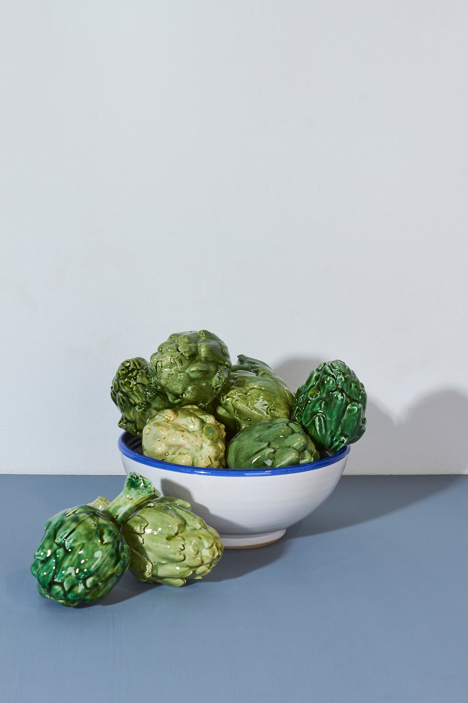 Tazón blanco con borde azul lleno de alcachofas verdes brillantes, decoración rústica y vibrante.
