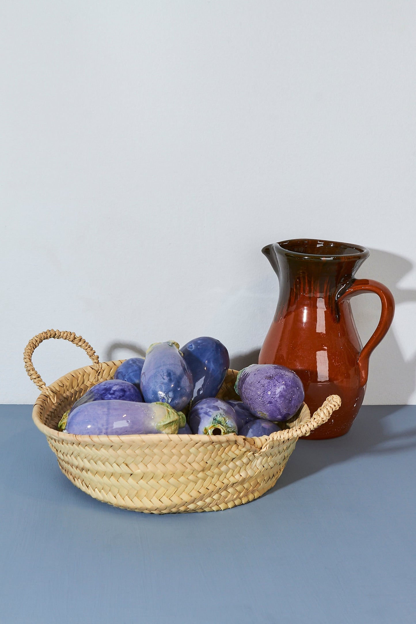 Cesta de mimbre con berenjenas moradas y jarrón de cerámica color marrón. Decoración rústica para cocina.