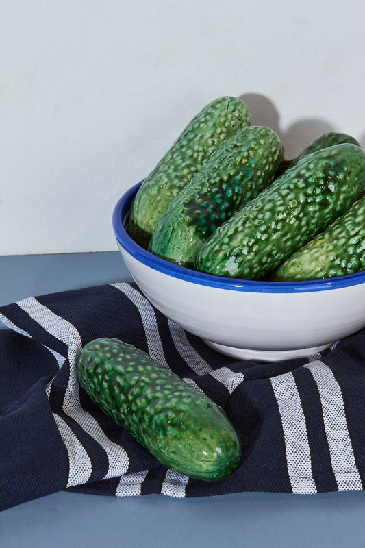Pepinos verdes brillantes en un tazón blanco y azul, sobre un paño de cocina a rayas negras y blancas.