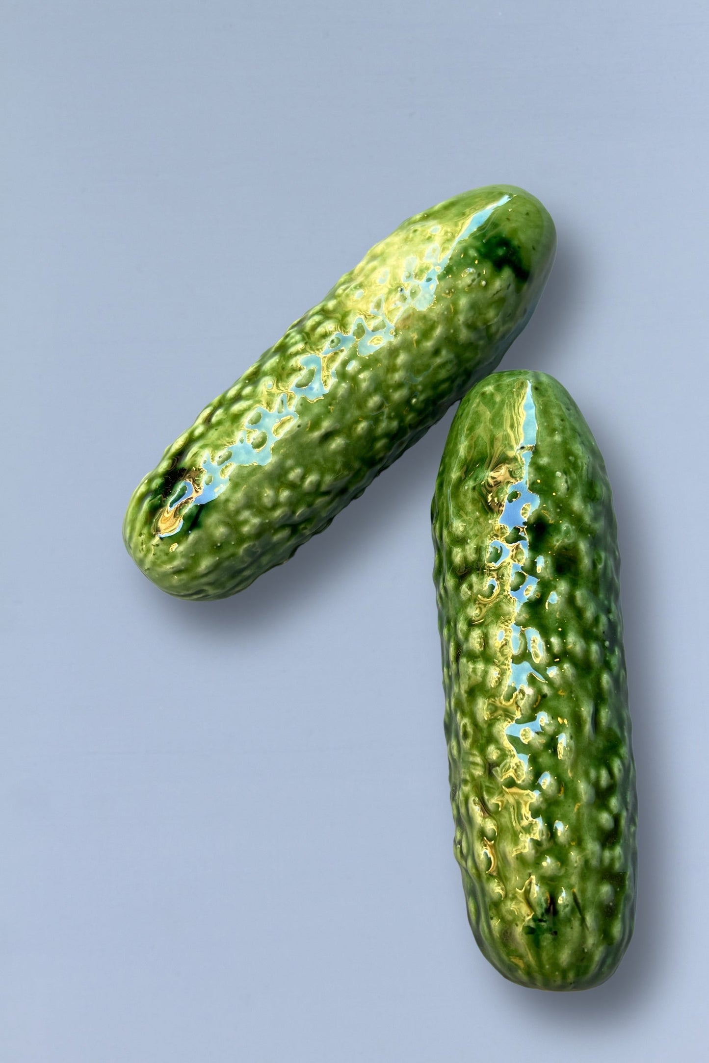 Dos pepinos de cerámica verde brillante con textura realista sobre fondo gris. Perfectos para decoración.