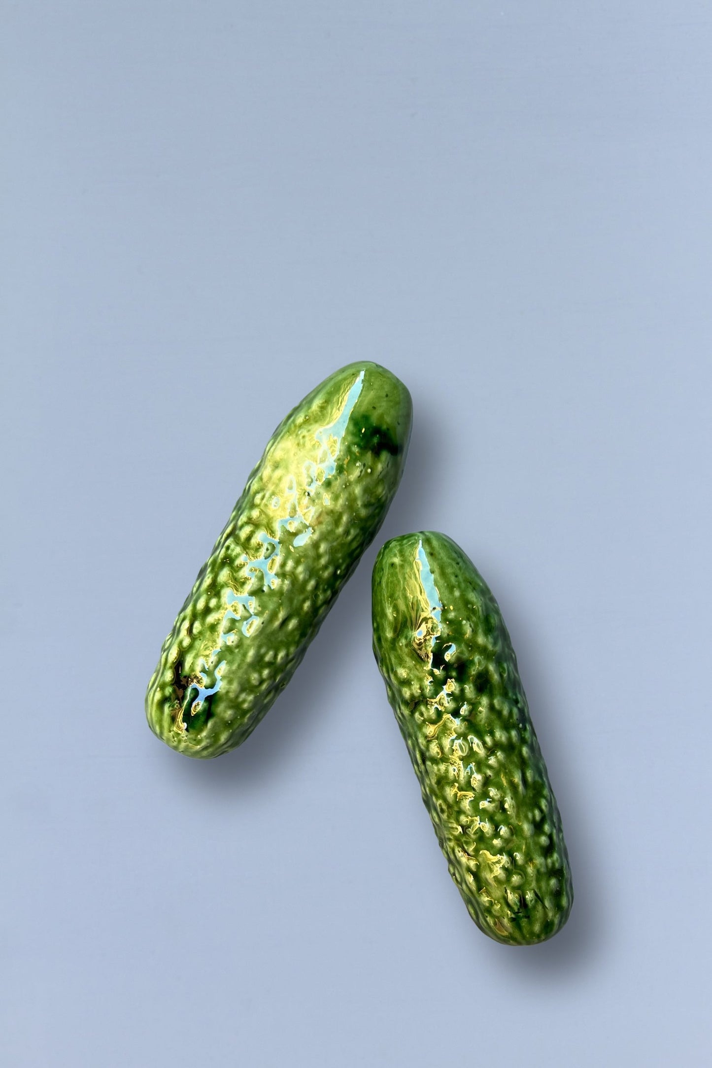 Dos pepinos de cerámica verde brillante, texturizados, ideales para decoración de cocina o como regalo.