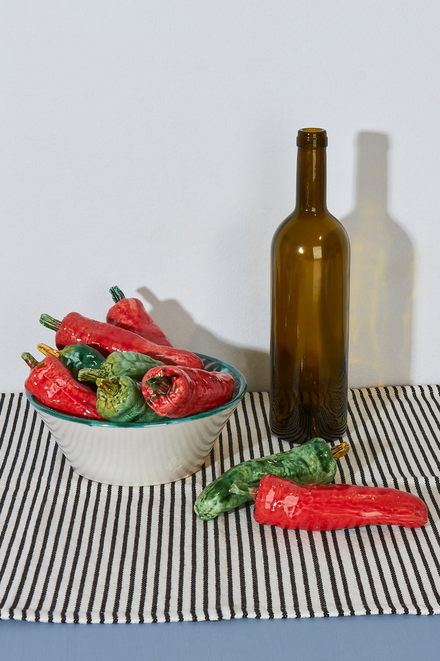 Plato cerámico blanco con chiles rojos y verdes, botella marrón en fondo de rayas blancas y negras.