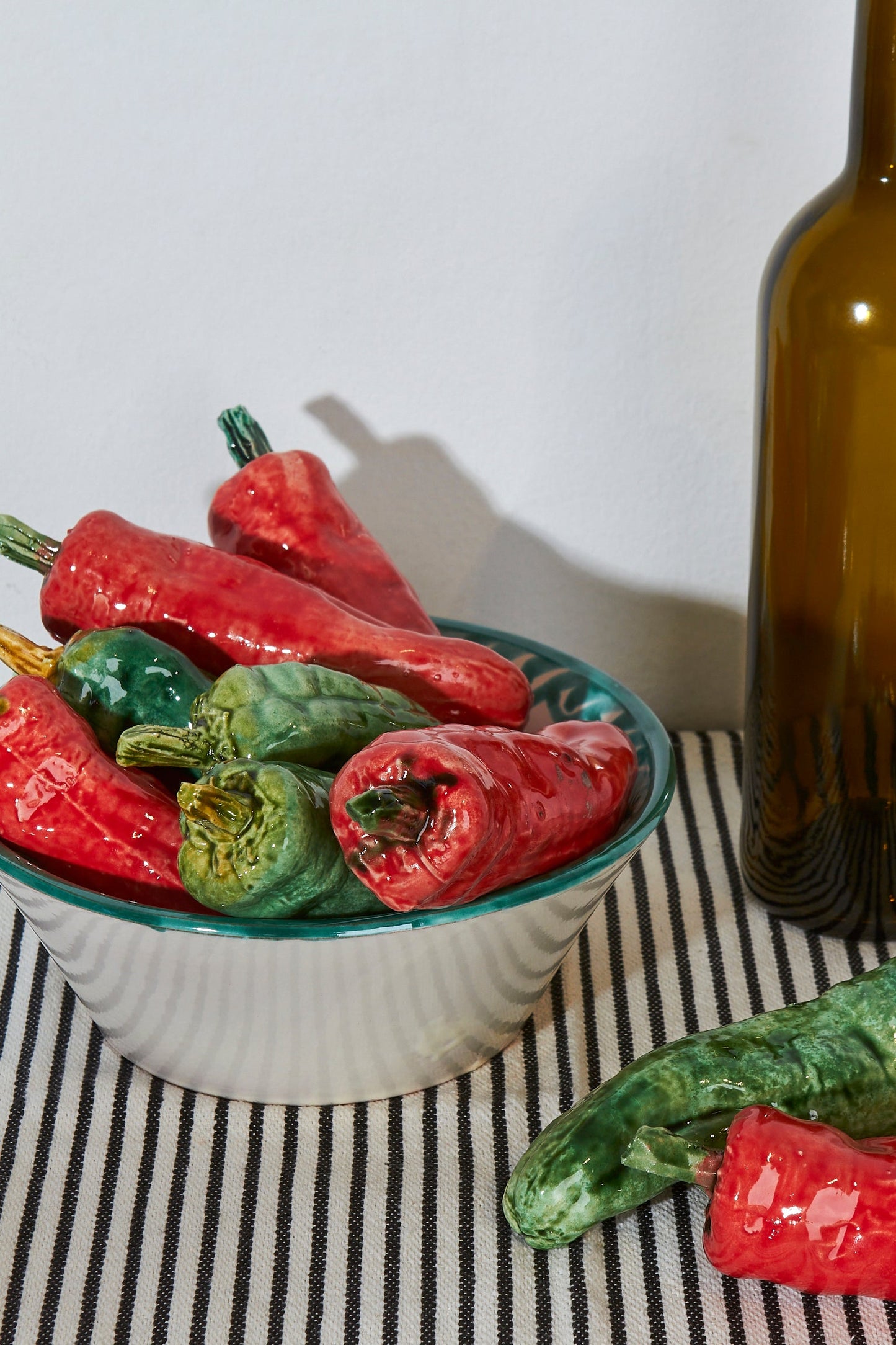 Tazón de cerámica con chiles rojos y verdes, acompañado de una botella marrón, sobre un fondo a rayas.