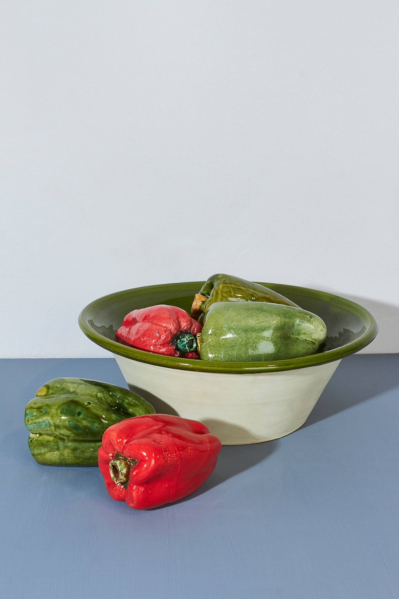Tazón cerámico beige con borde verde, lleno de pimientos rojos y verdes. Ideal para servir comidas.