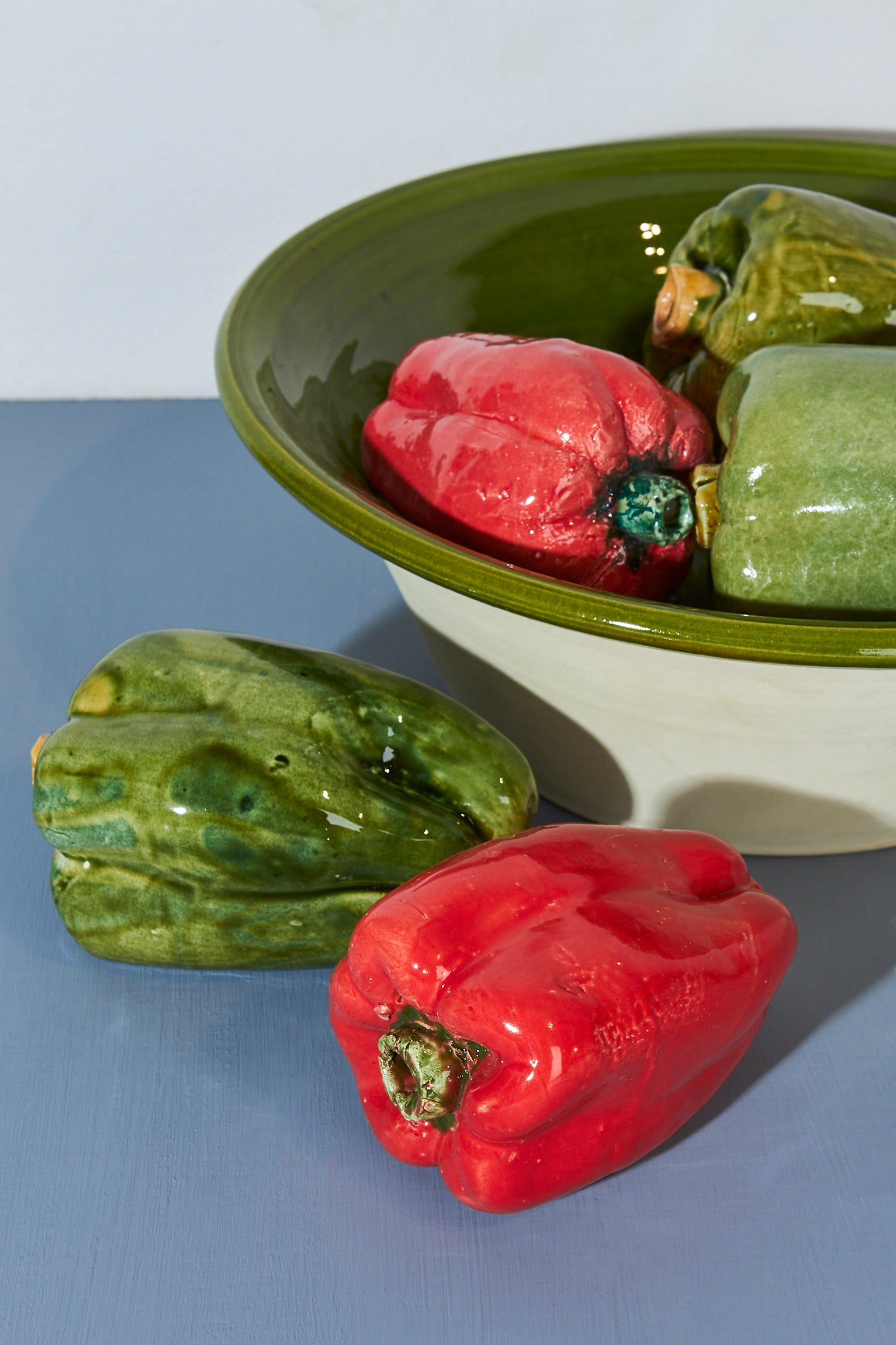 Pimientos de cerámica en colores verde y rojo dentro de un tazón de cerámica verde. Estilo artesanal y decorativo.