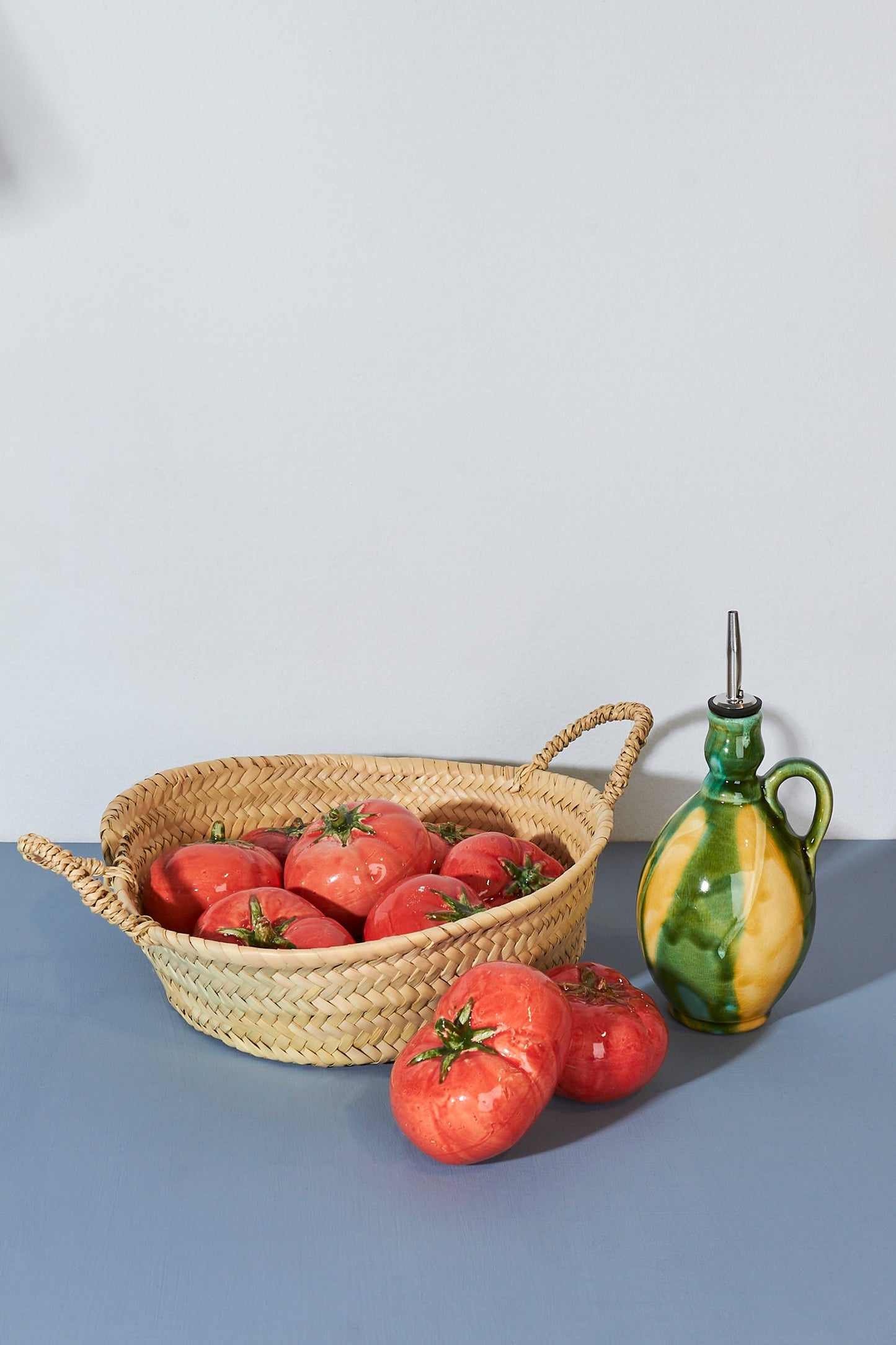 Cesta de mimbre con tomates rojos y jarra de cerámica verde y amarilla. Ideal para decoración rústica.