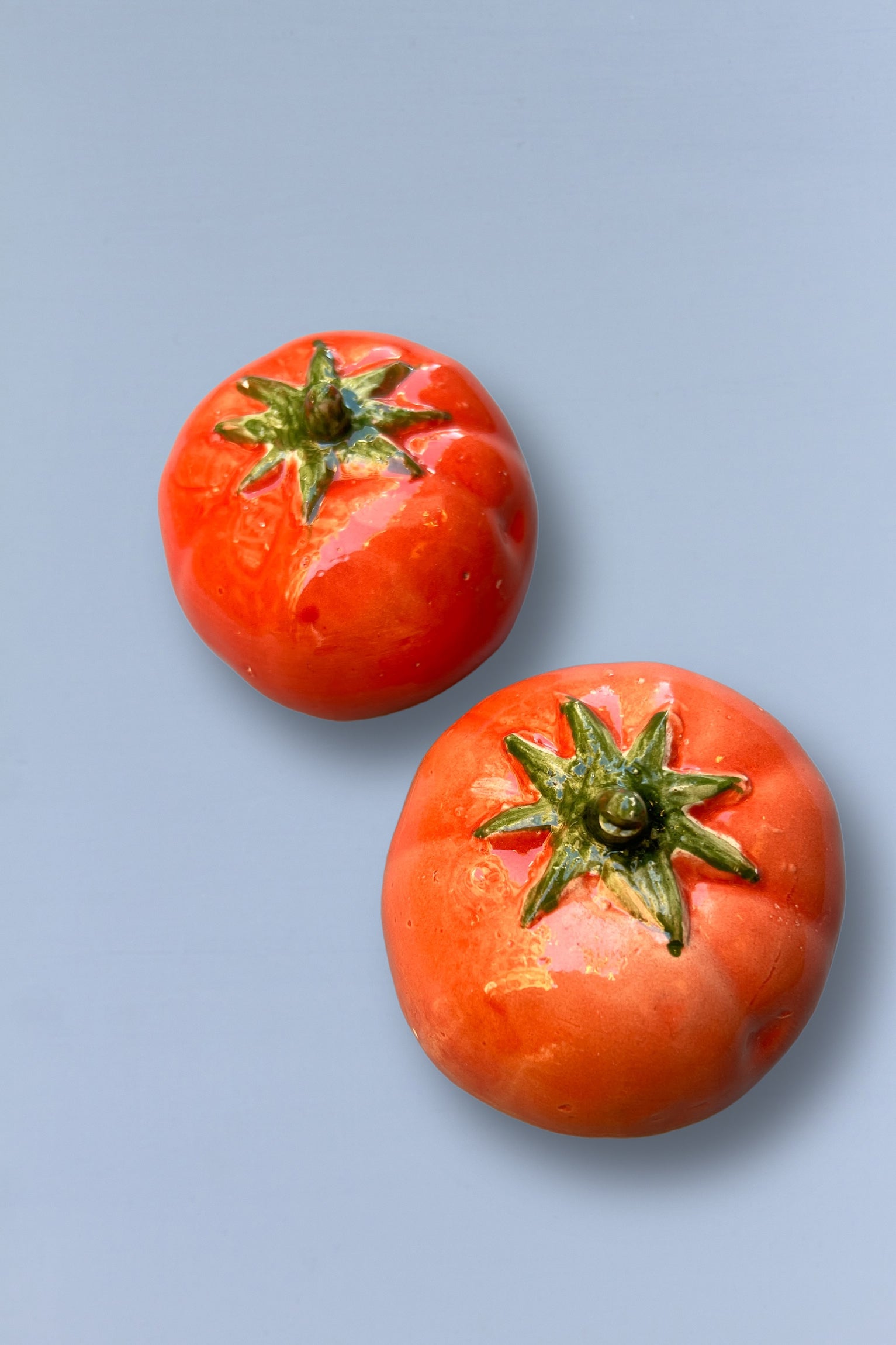 Tomates de cerámica roja brillante, decorativos, con detalles verdes, ideales para adornar mesas o cocinas.
