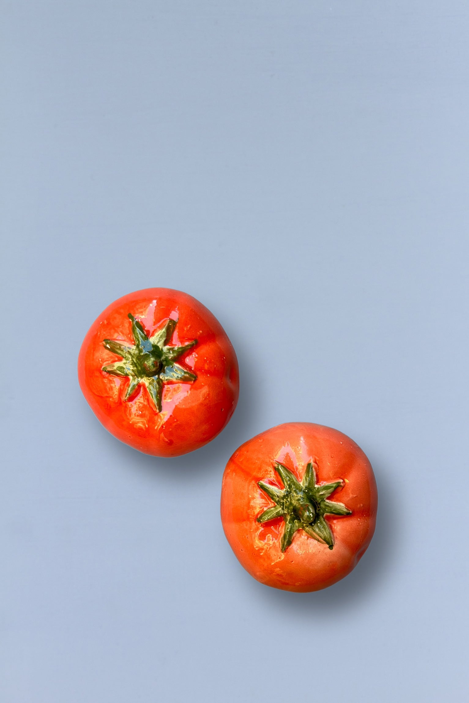 Dos tomates rojos brillantes sobre fondo azul claro, con detalles realistas en la textura y forma.