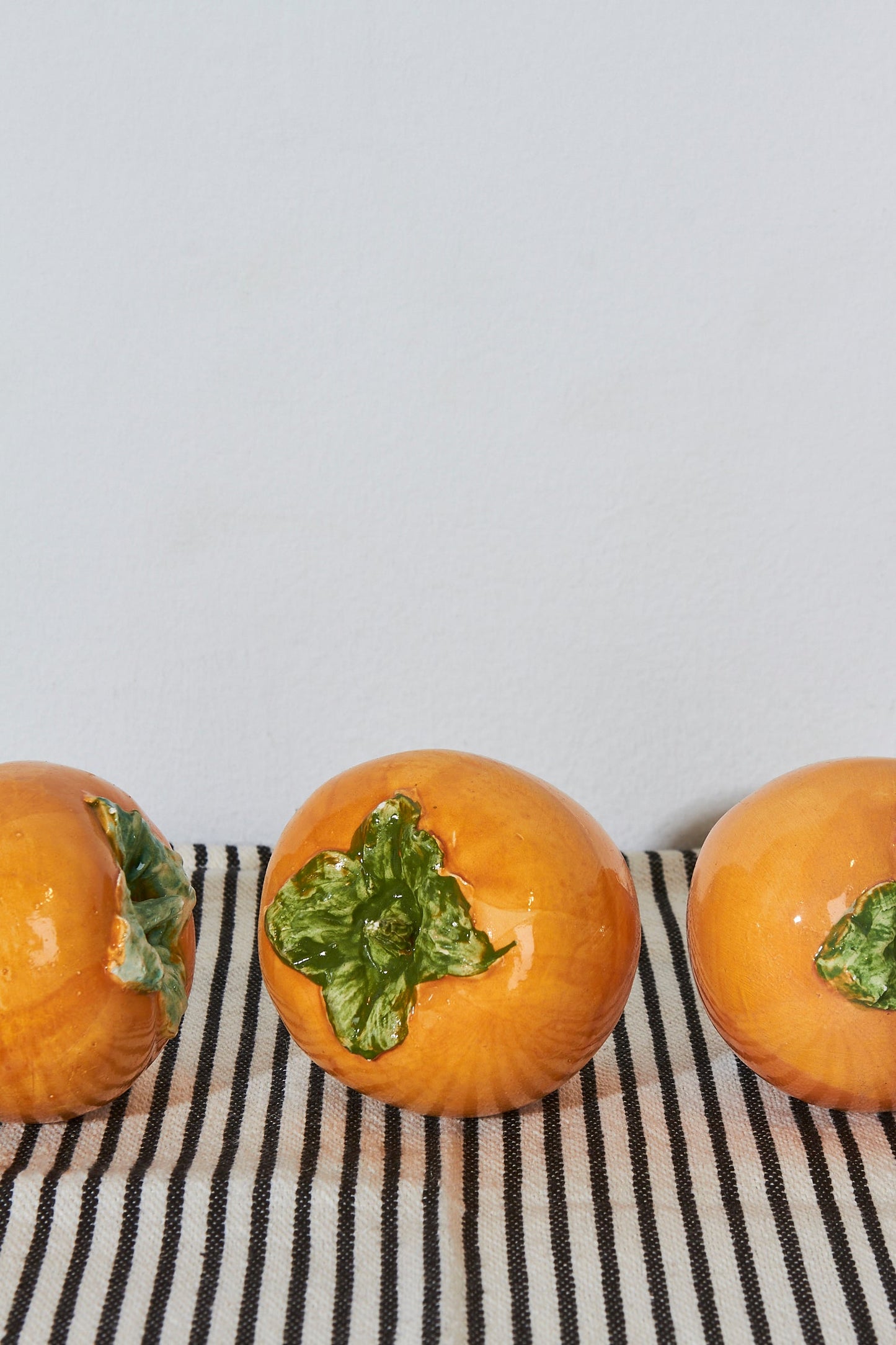 Tres decorativas calabazas de cerámica naranja con detalles en verde sobre una tela a rayas.