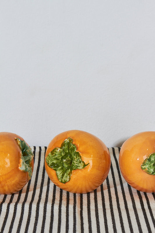 Tres decorativas calabazas de cerámica naranja con detalles en verde sobre una tela a rayas.