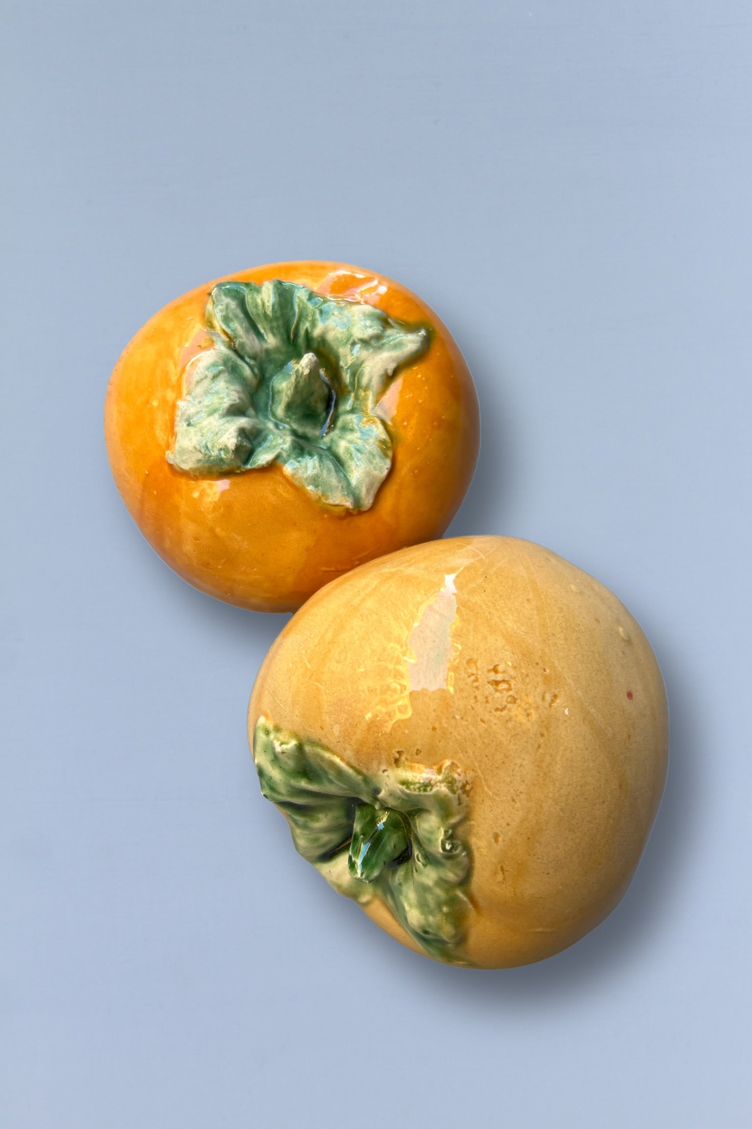 Jarrón de cerámica en forma de caqui, color naranja y verde, estilo moderno y decorativo.