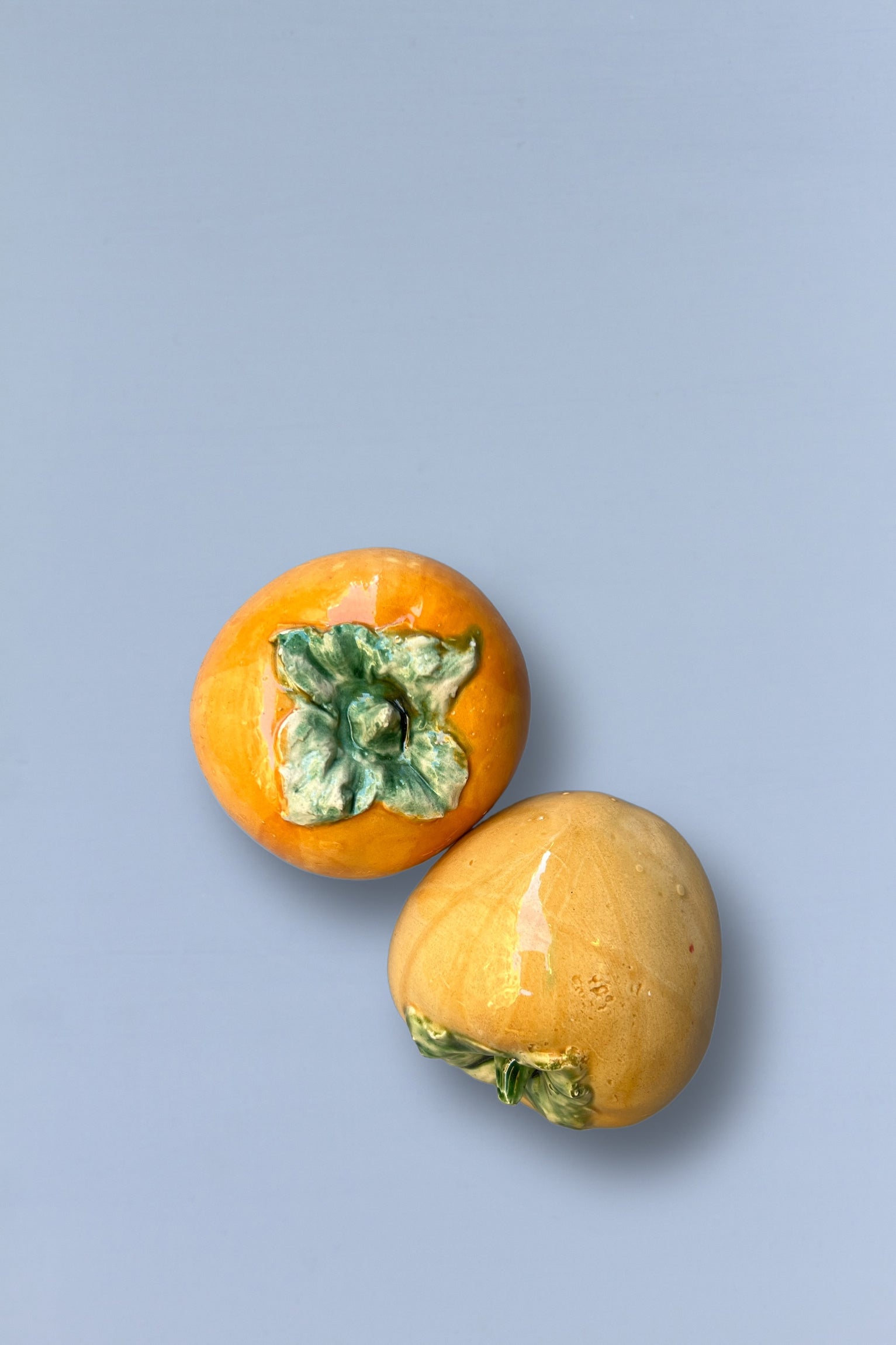 Frutas persimonas amarillas con hojas verdes en fondo azul claro, decorativas y realistas.