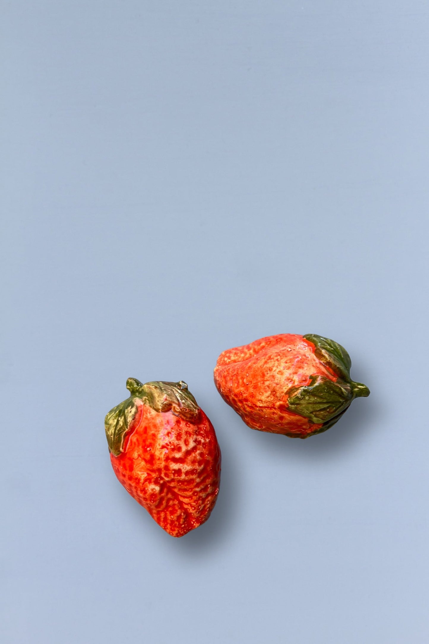 Fresas decorativas de cerámica roja y verde sobre fondo azul. Ideal para decoración de cocina.