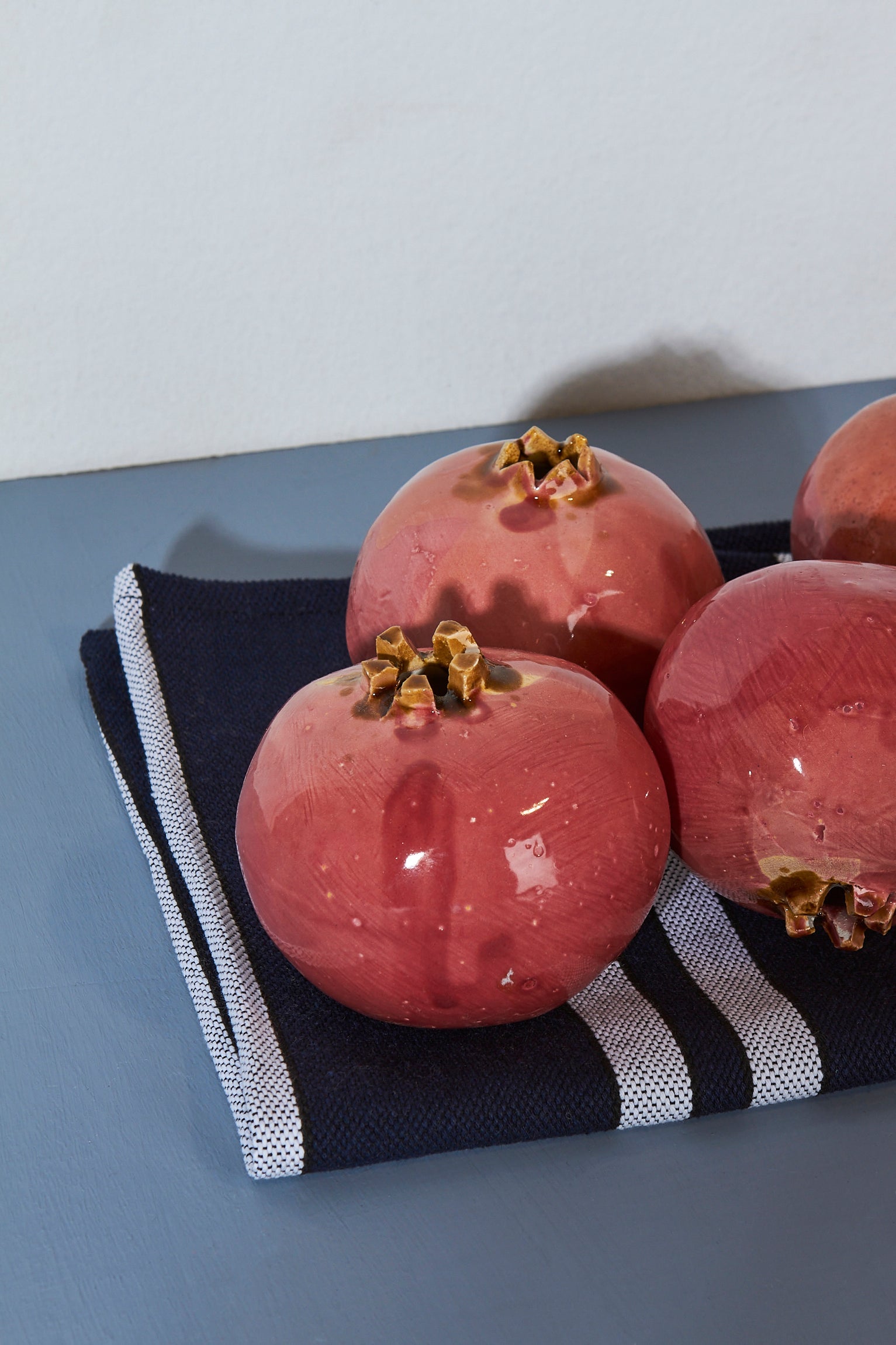 Frutas de granada cerámica rojas en un paño de cocina azul marino con rayas blancas. Ideal para decoración.