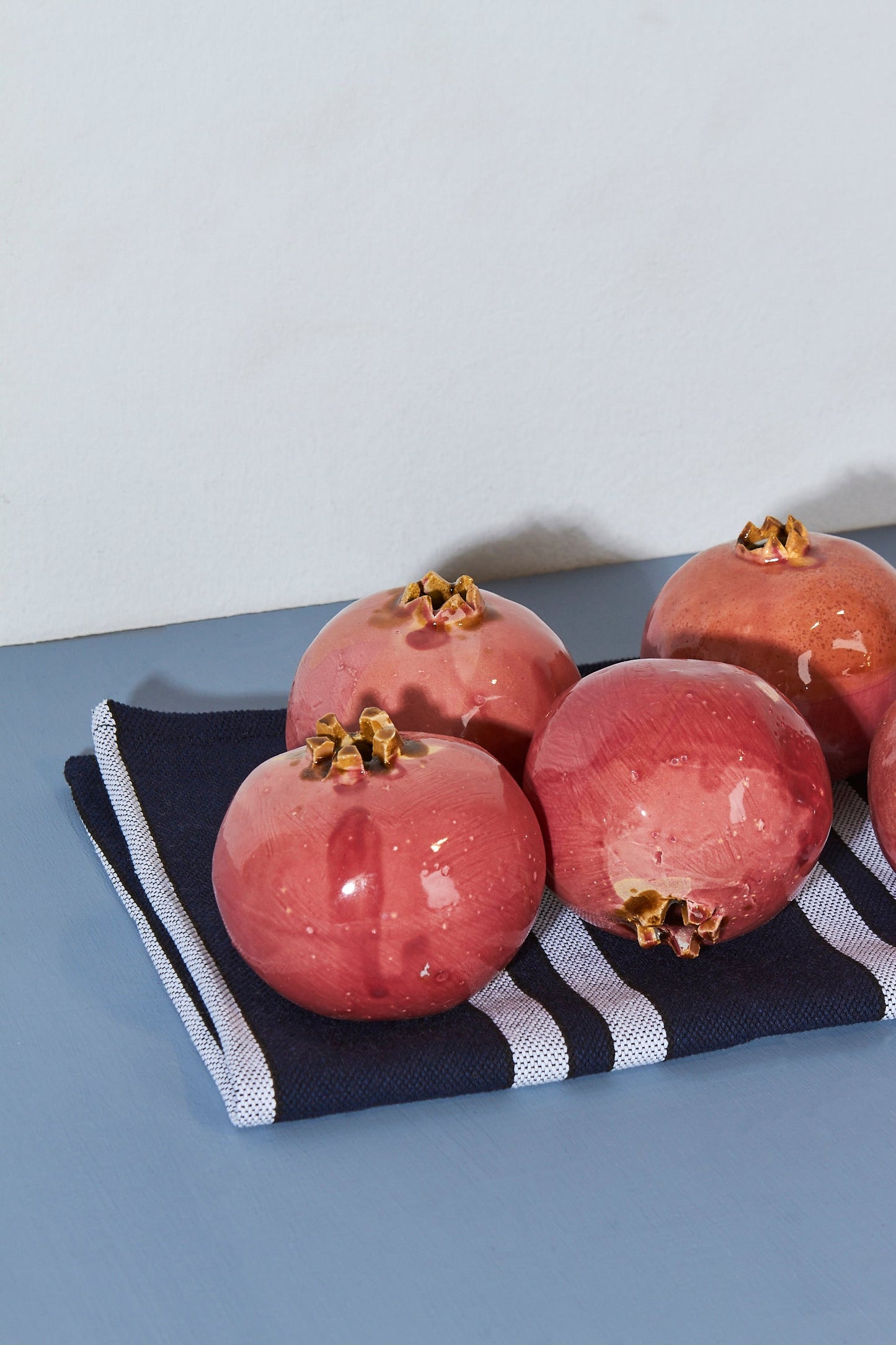 Granadas cerámicas de color rojo brillante sobre un paño de cocina azul y blanco a rayas.