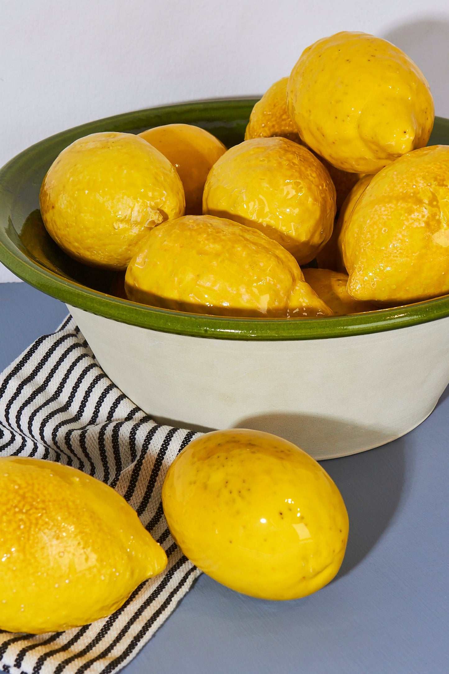 Limones amarillos brillantes en un tazón de cerámica verde con borde beige, sobre un paño blanco y negro a rayas.