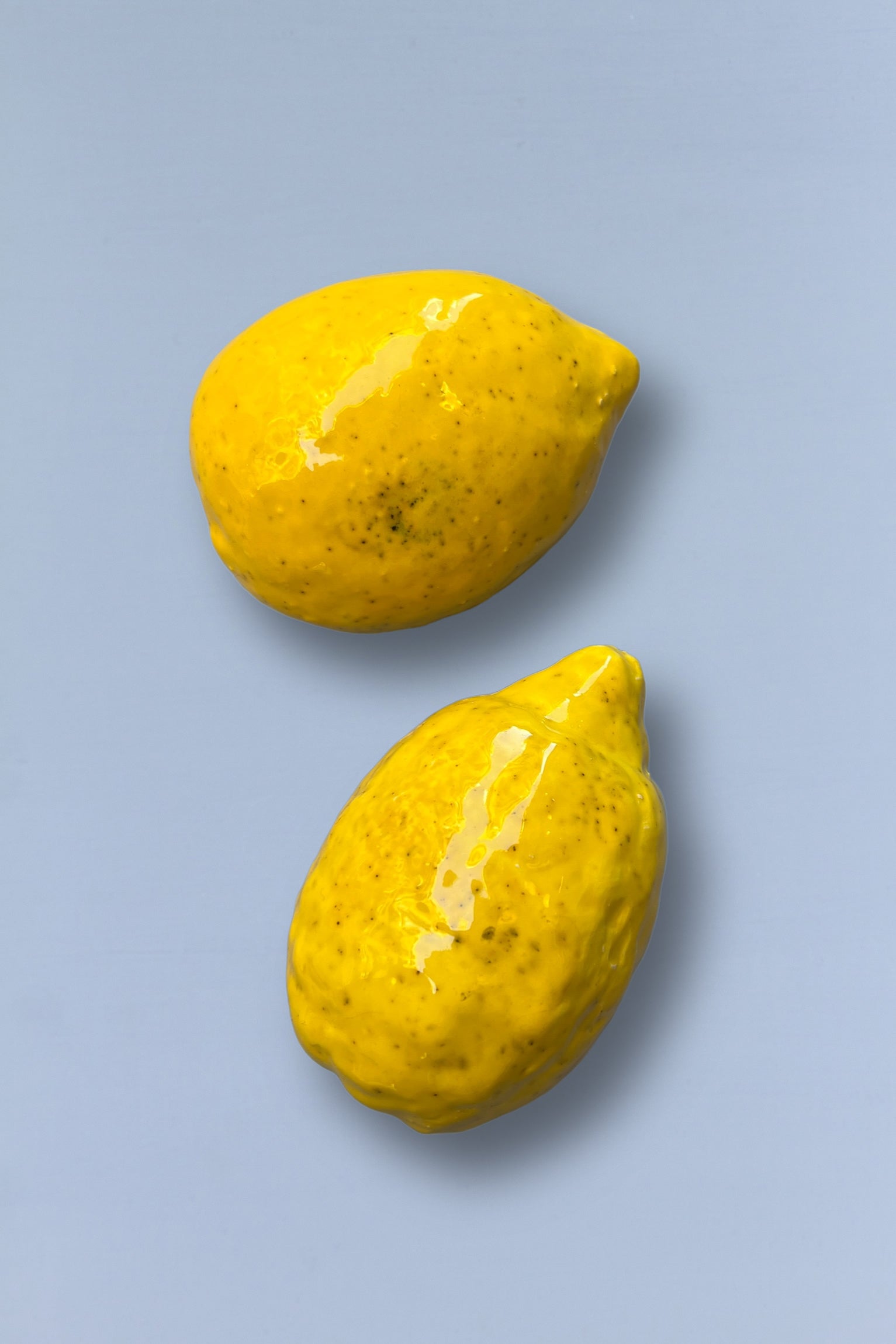 Limones cerámicos amarillos brillantes, decorativos, sobre fondo azul claro, estilo moderno y artesanal.