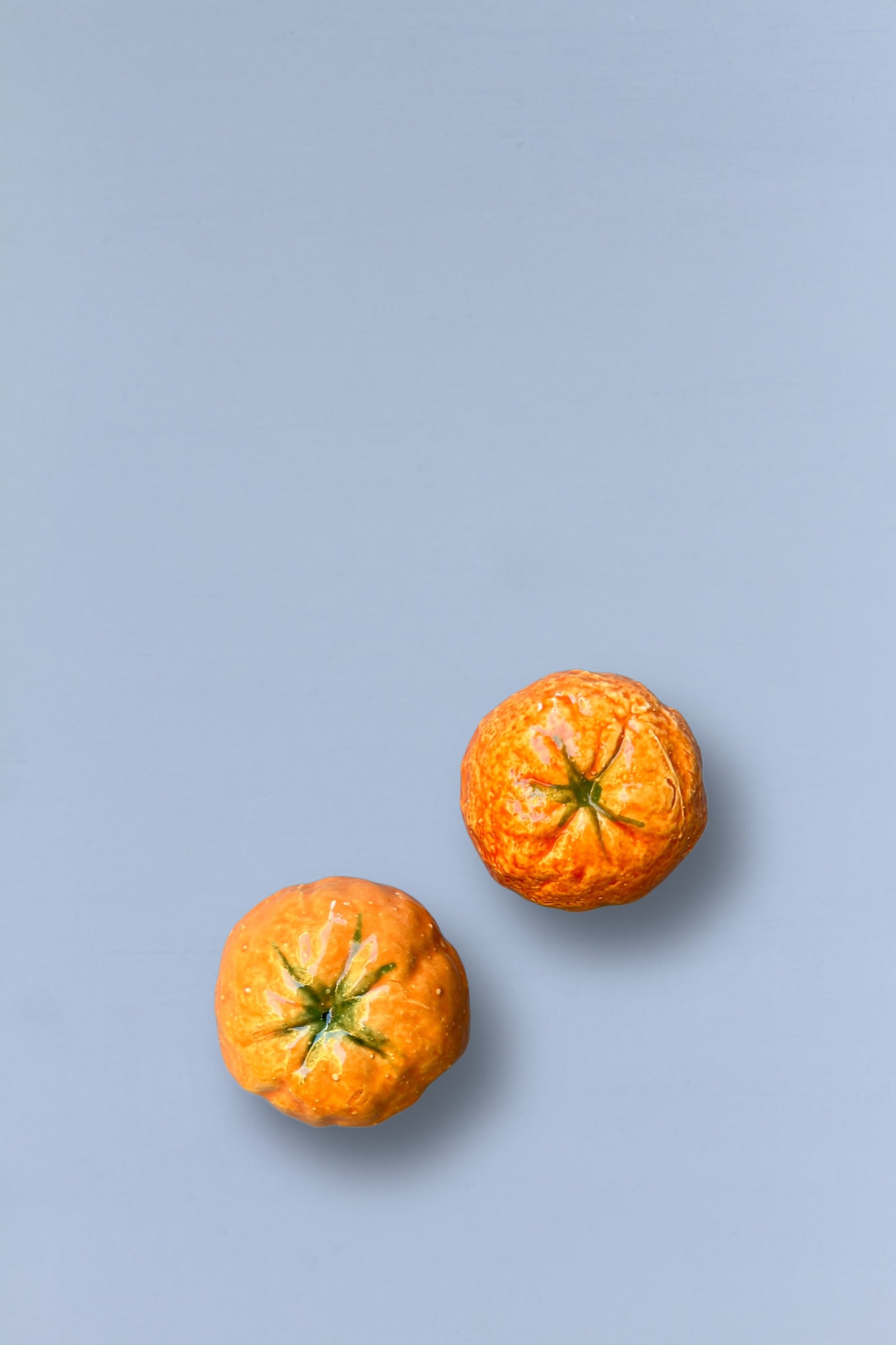 Dos mandarina pequeñas, color naranja brillante con textura rugosa, sobre un fondo azul suave.