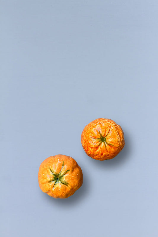 Dos mandarina pequeñas, color naranja brillante con textura rugosa, sobre un fondo azul suave.