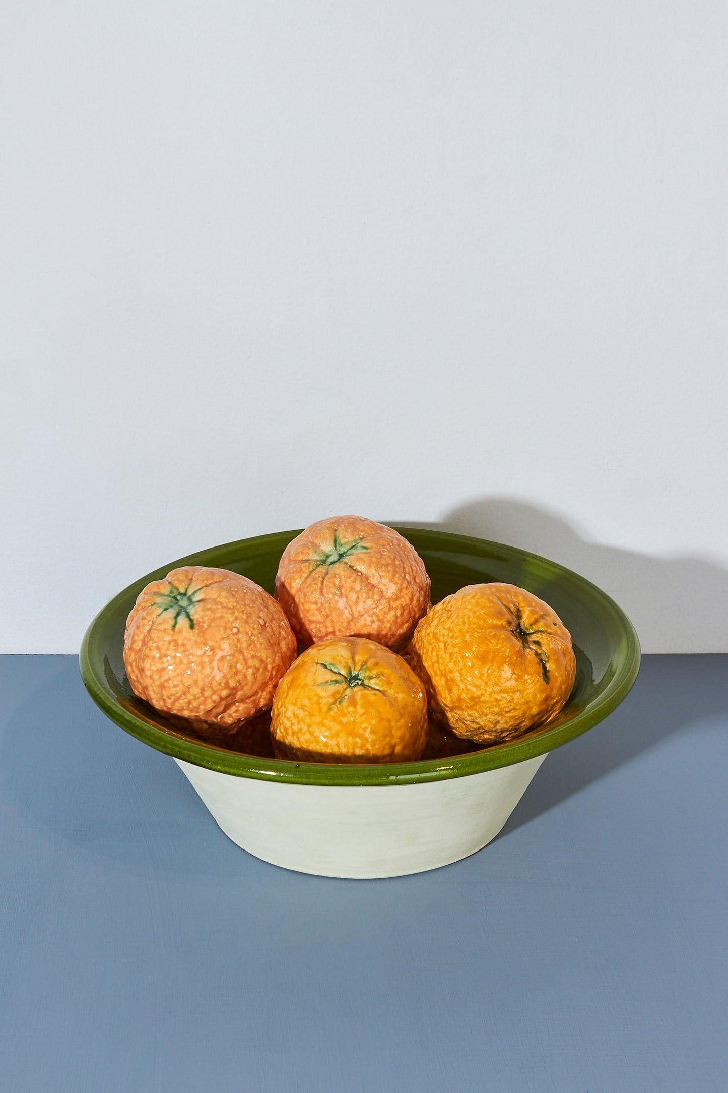 Cuenco cerámico blanco con borde verde, lleno de naranjas marrones y amarillas, estilo vintage.