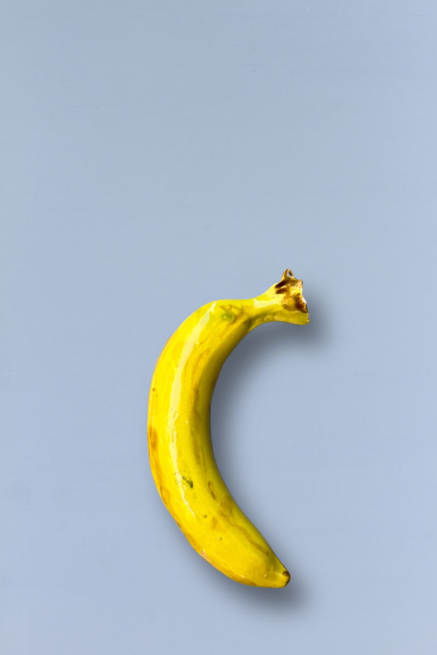 Plátano amarillo brillante sobre fondo gris, hecho de cerámica, estilo moderno y decorativo.