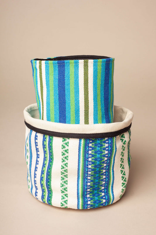 Dos cestos cilíndricos de tela tejida con rayas y motivos geométricos en tonos azul, verde y blanco. Borde negro.