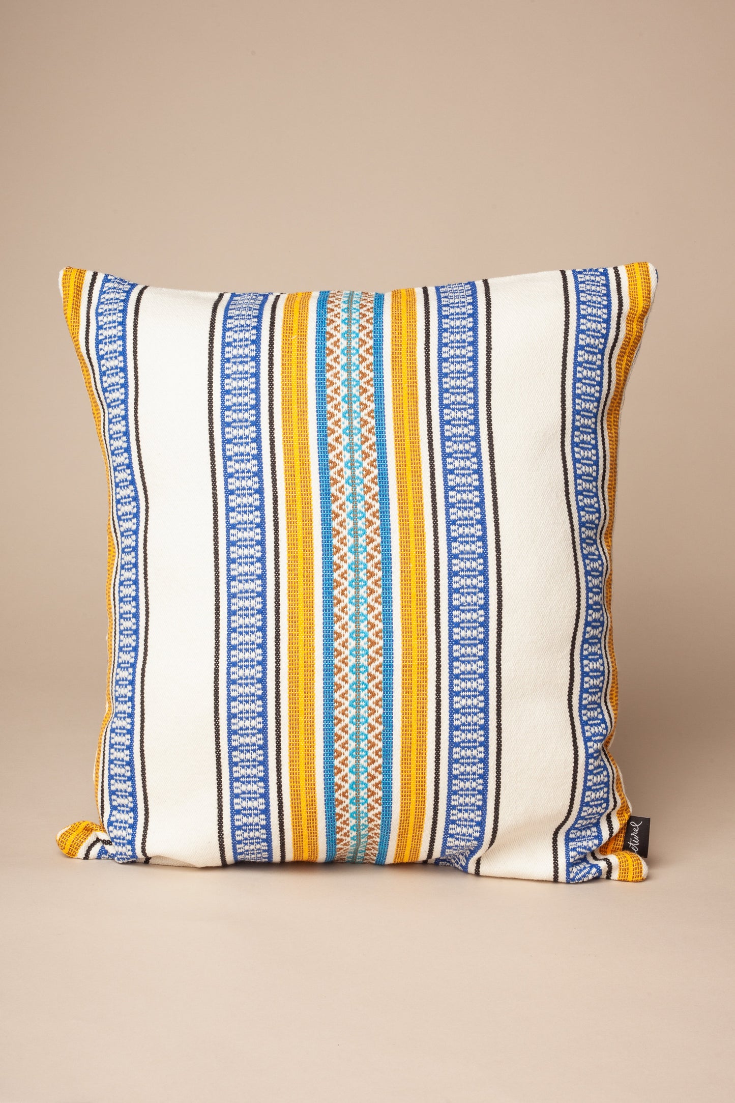 Cojín cuadrado de algodón blanco con rayas azules, amarillas y detalles en turquesa, estilo boho chic.