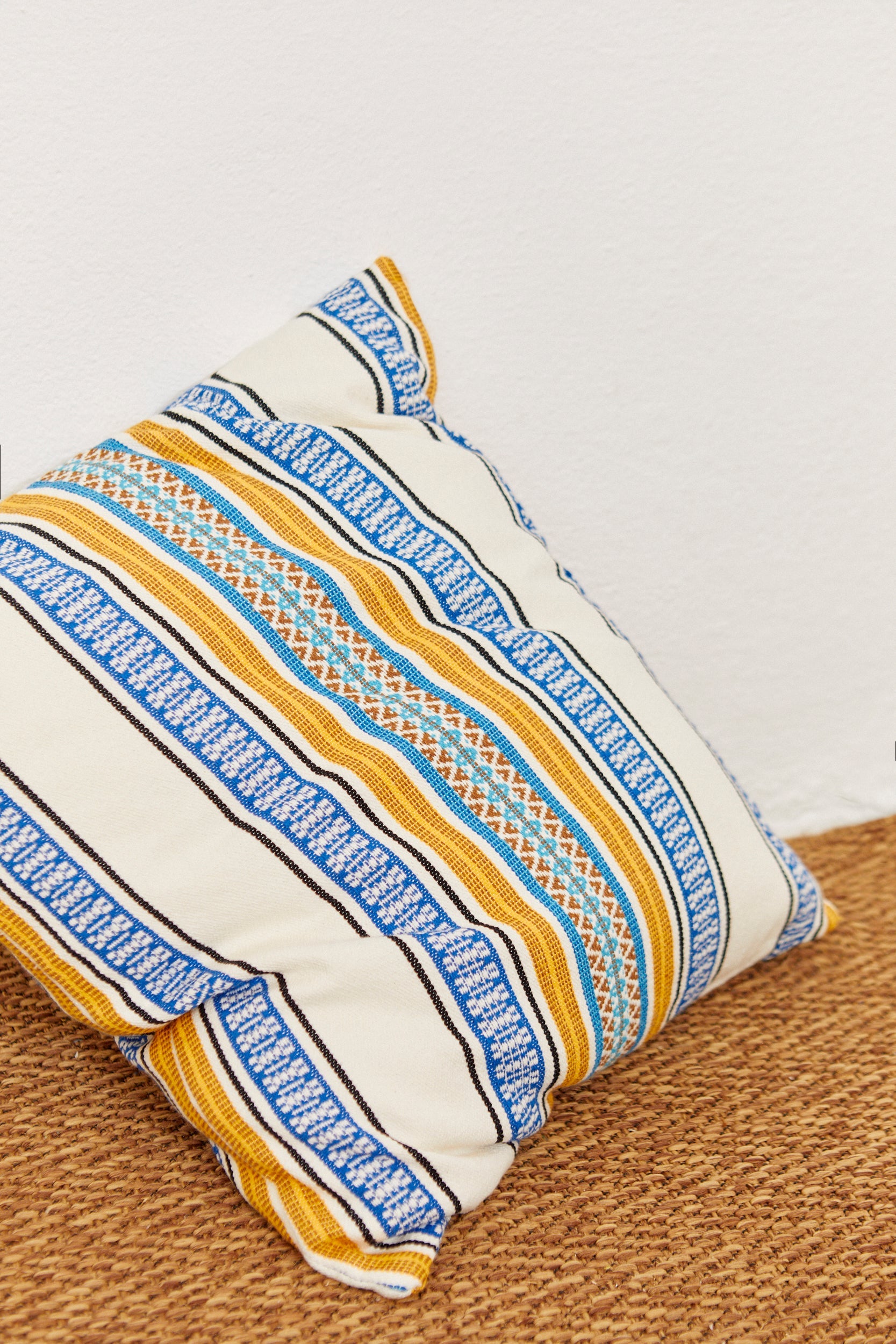 Cojín cuadrado de algodón color crema con estampado azul y amarillo, estilo bohemio, perfecto para decoración.
