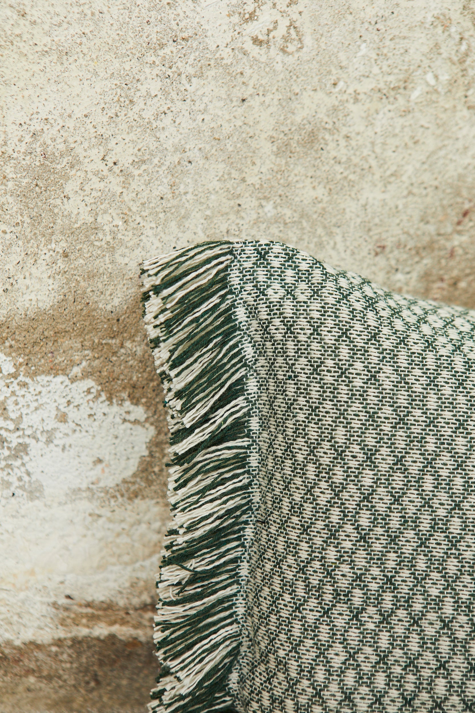 Cojín verde con diseño de cuadros y flecos, ideal para decoración rústica y contemporánea.