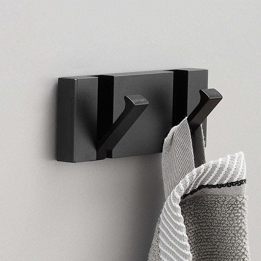 Perchero de pared moderno de metal negro mate con dos ganchos, sosteniendo una toalla gris sobre pared clara.