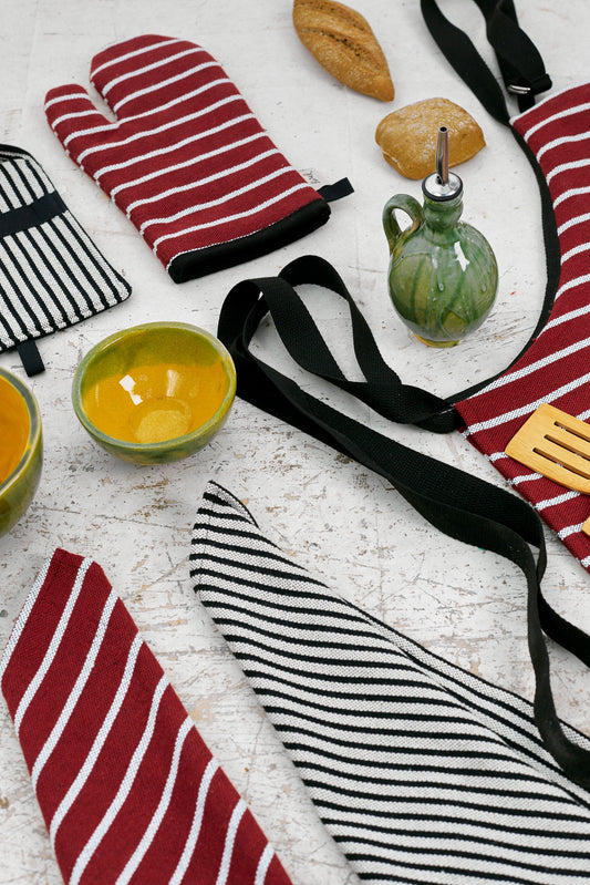 Juego de cocina con guantes rojos y negros a rayas, delantal y utensilios en tonos verdes y amarillos.