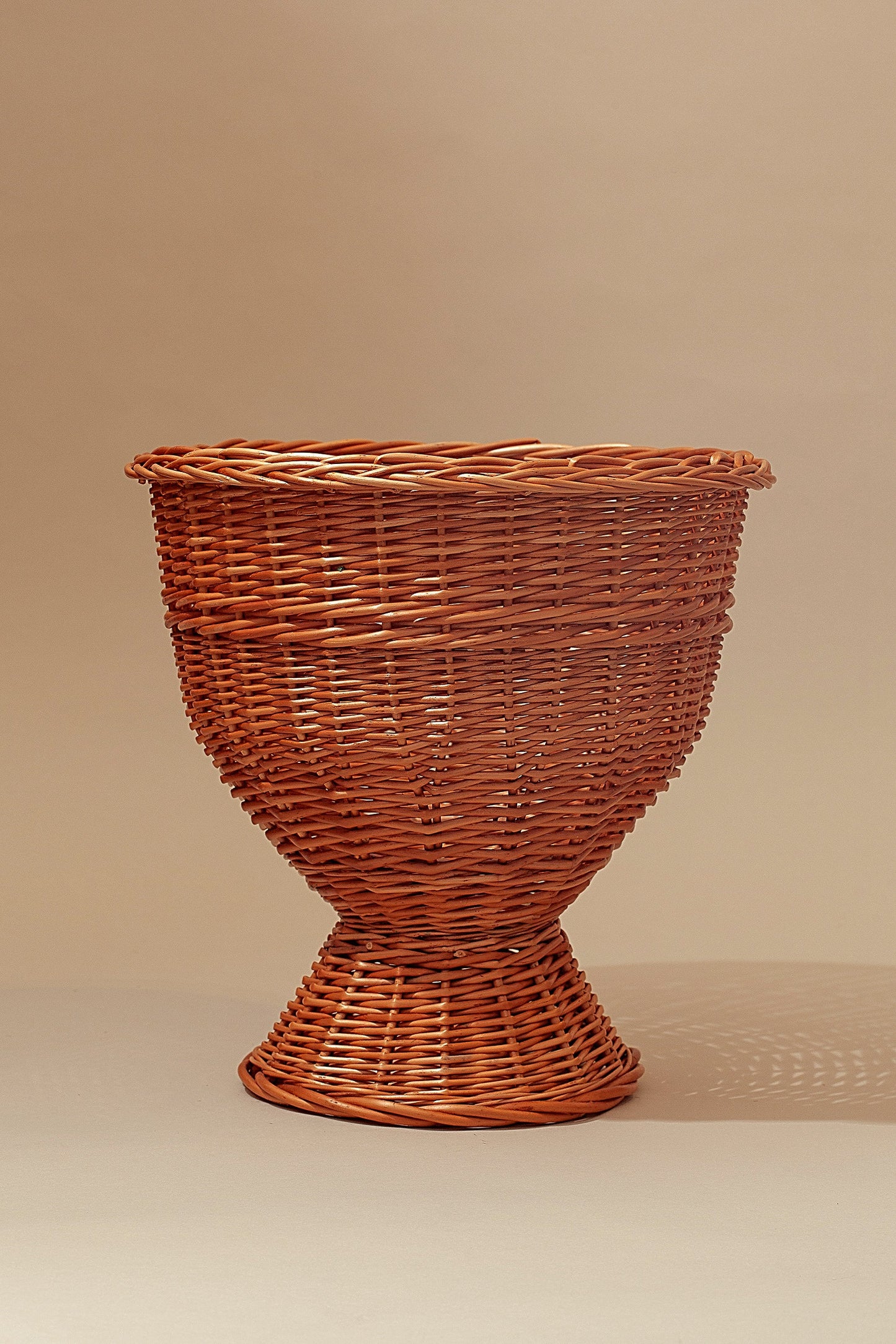 Cesta trenzada de mimbre marrón, estilo moderno, con base amplia y diseño elegante para decoración.