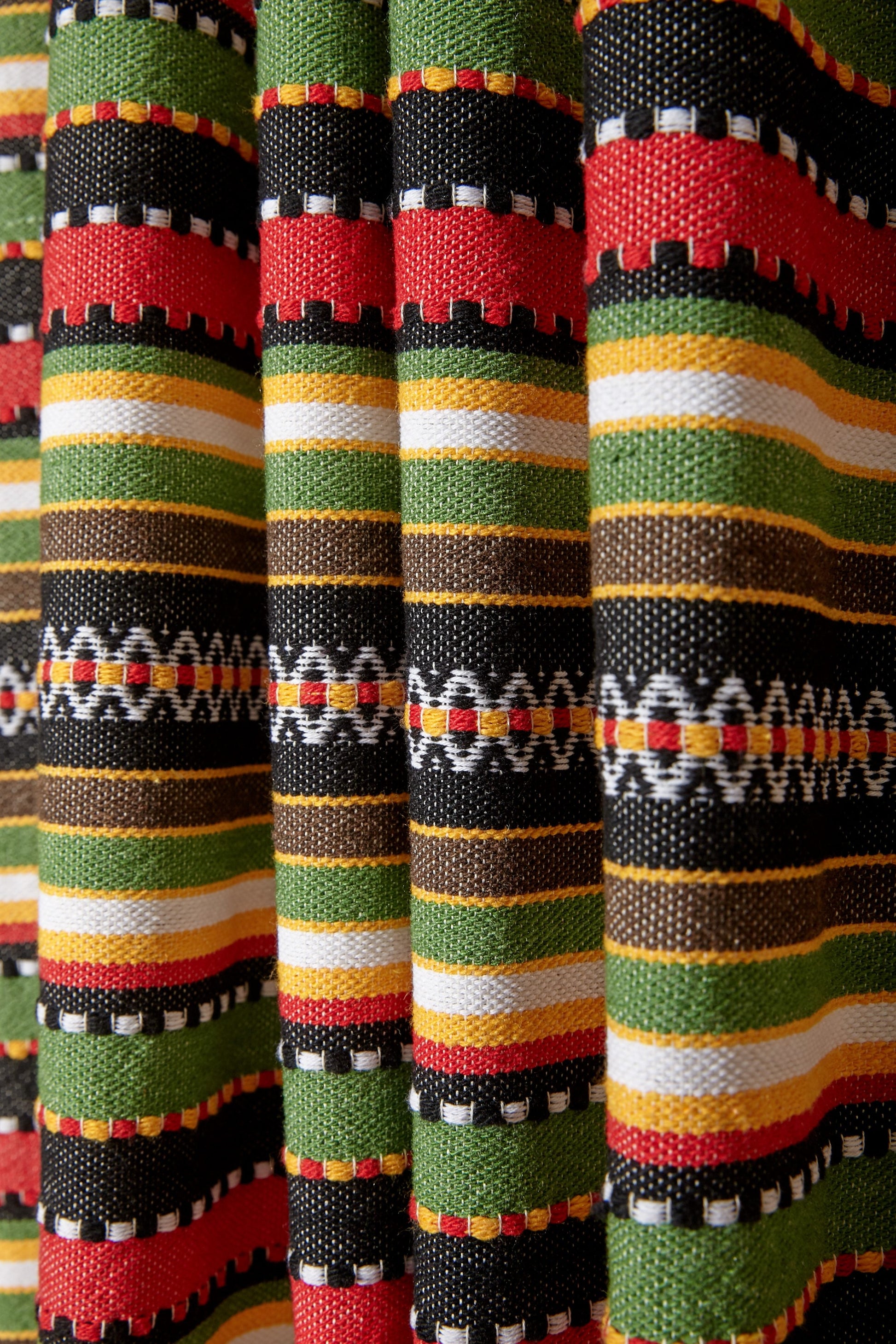 Tela de algodón en tonos rojo, verde, negro y amarillo con diseño de rayas, ideal para decoración o confección.