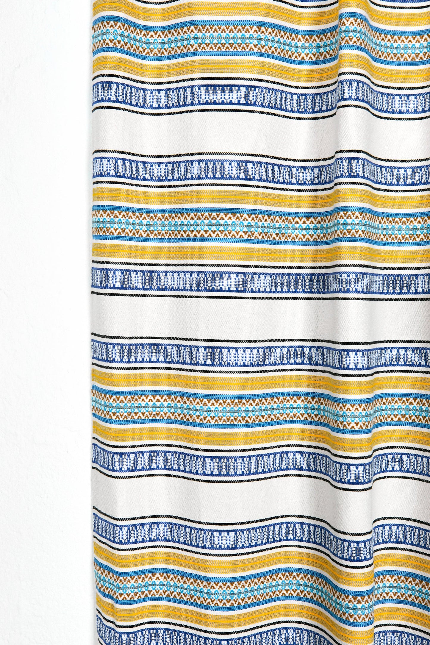 Cortina de tela blanca con rayas amarillas, azules y patrones geométricos, ideal para decorar cualquier habitación.