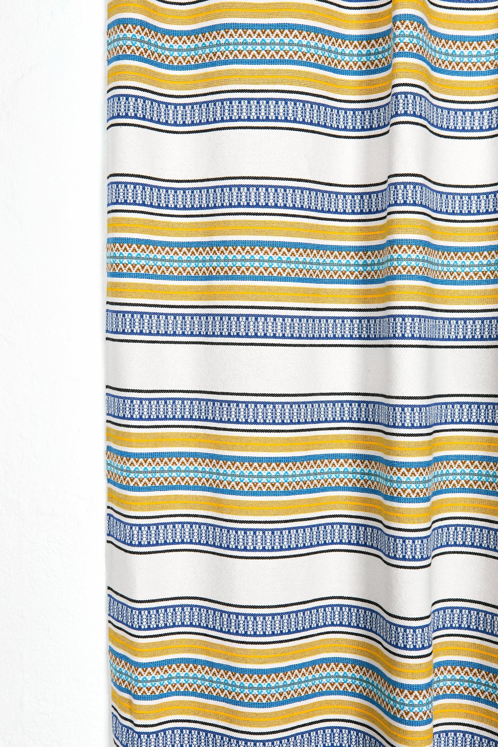 Cortina de tela blanca con rayas amarillas, azules y patrones geométricos, ideal para decorar cualquier habitación.