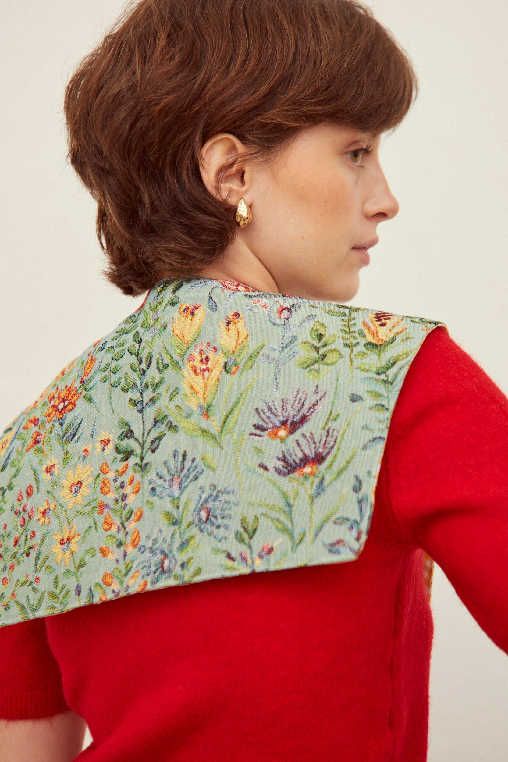 Cuello falso tejido estilo jacquard sobre fondo celeste con estampado de flores coloridas, usado sobre suéter rojo.