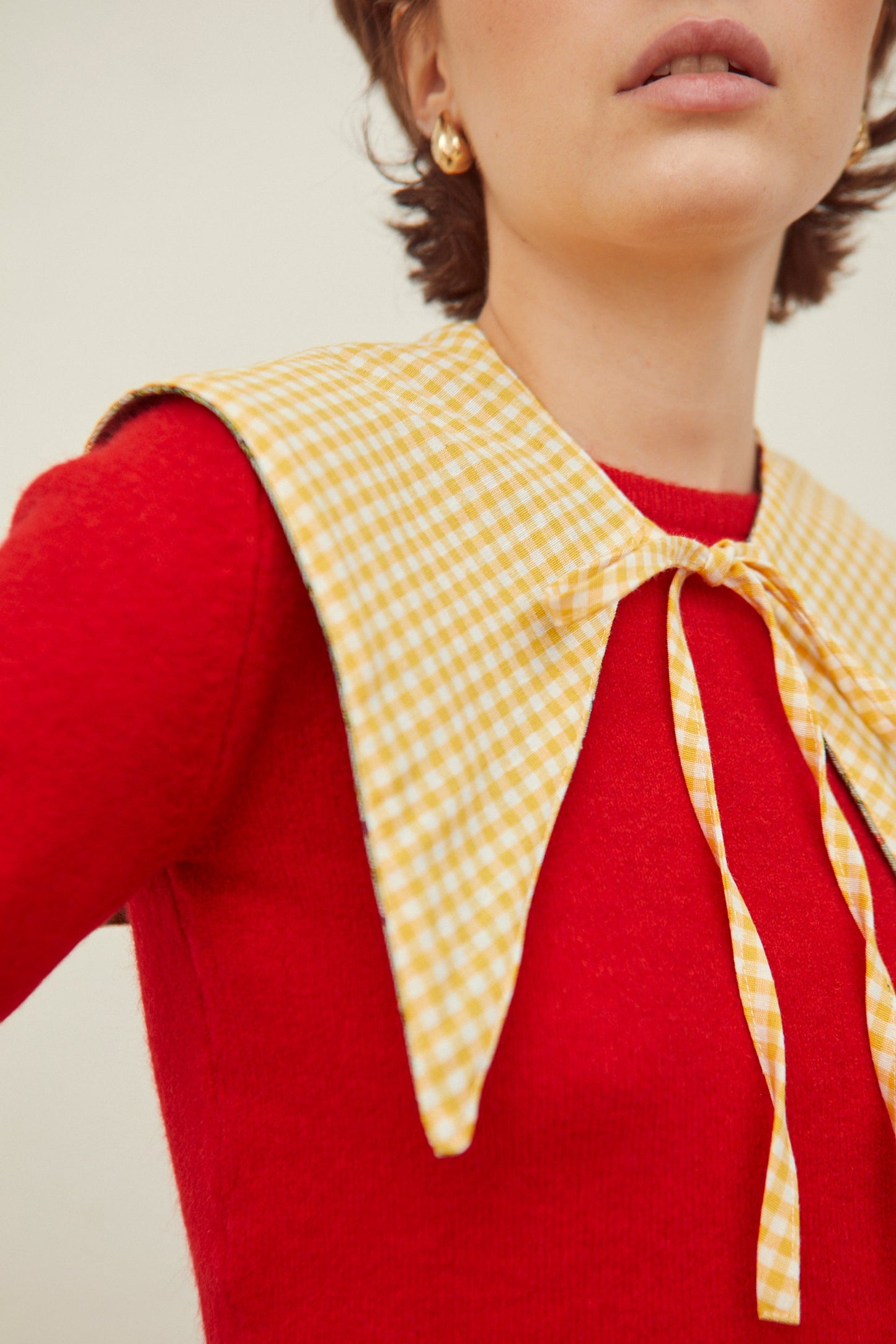 Cuello falso de tela a cuadros vichy amarillos con lazada frontal, sobre un suéter rojo de textura suave.