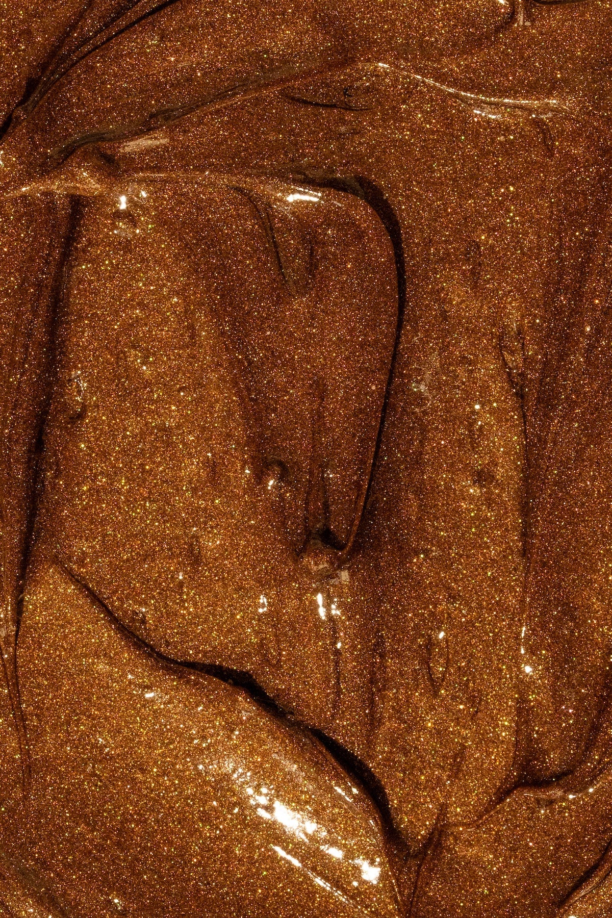 Shimmering, metallic hazelnut-brown lip balm with a smooth, glossy texture and fine golden glitter.