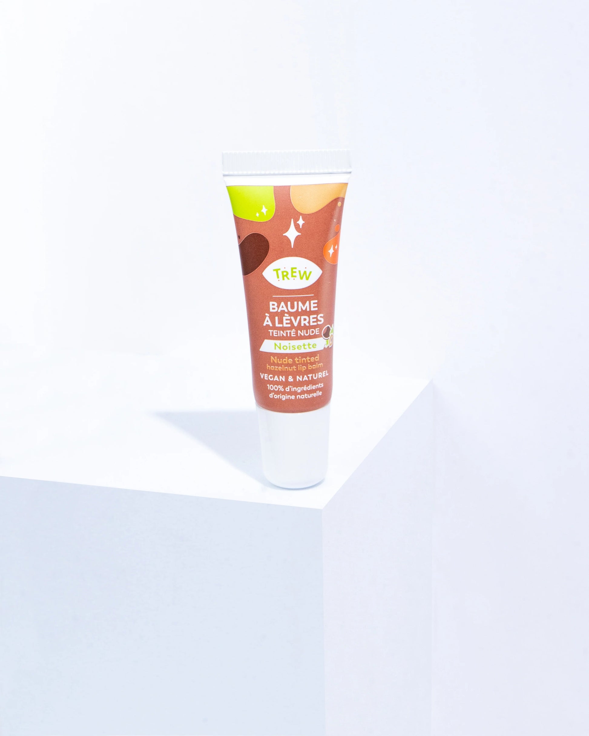 Trew Cosmetic nude tinted hazelnut lip balm in a squeeze tube with playful brown and white graphic patterns.