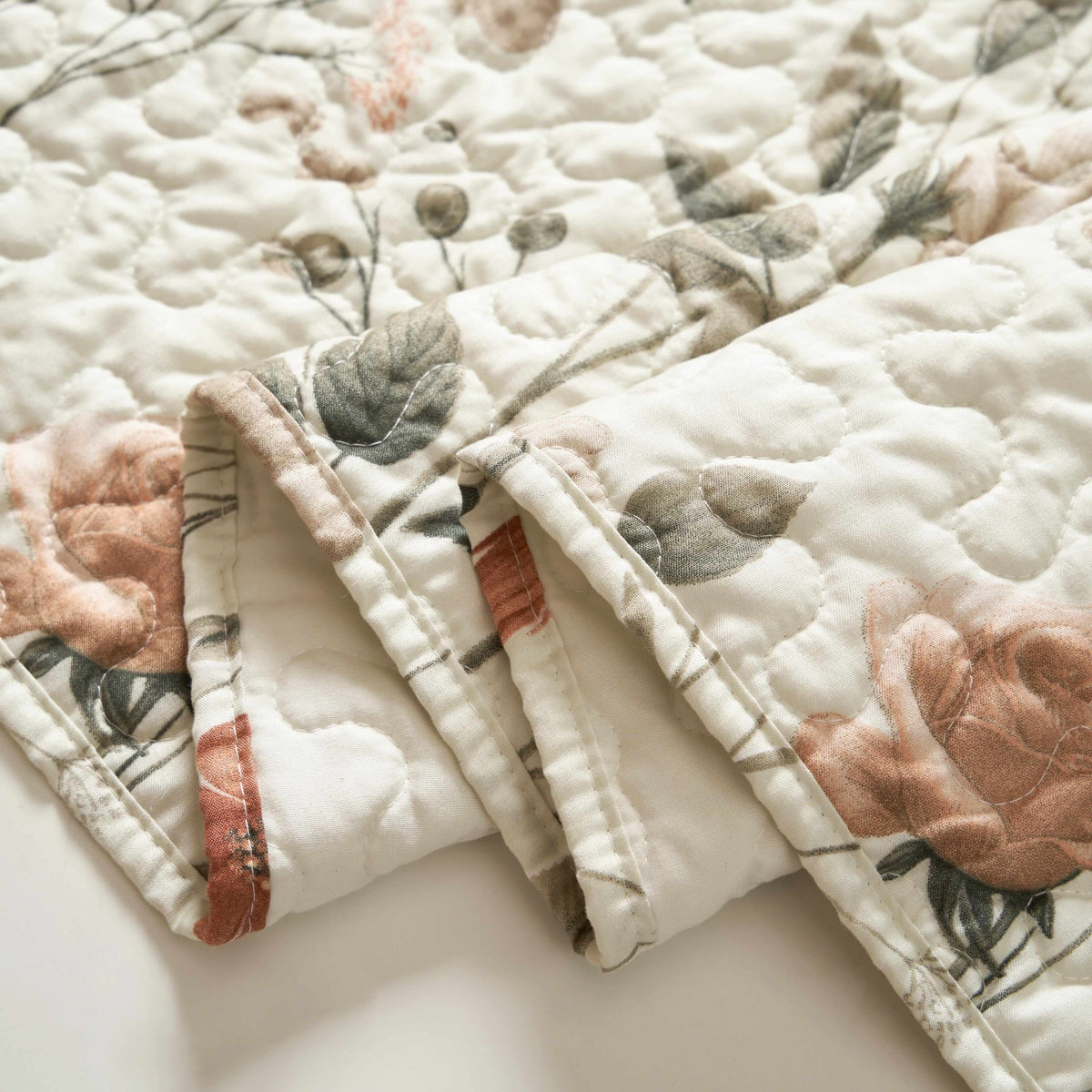 Quilted microfiber table runner in beige with rose flowers and soft olive green leaves in a folded, elegant pattern.