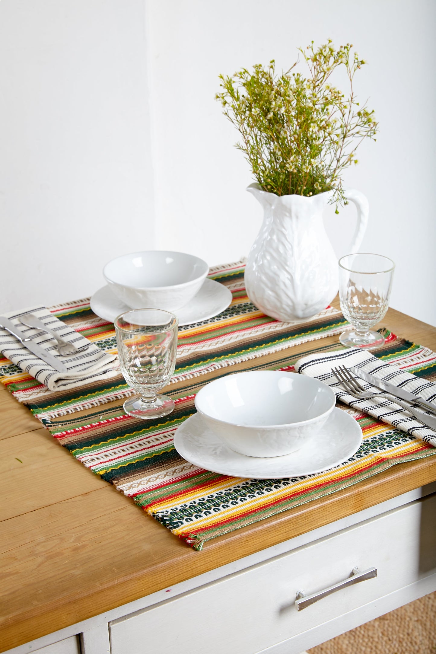 Mantel de mesa multicolor en rayas, hecho de algodón, con platos blancos y jarra de cerámica blanca.