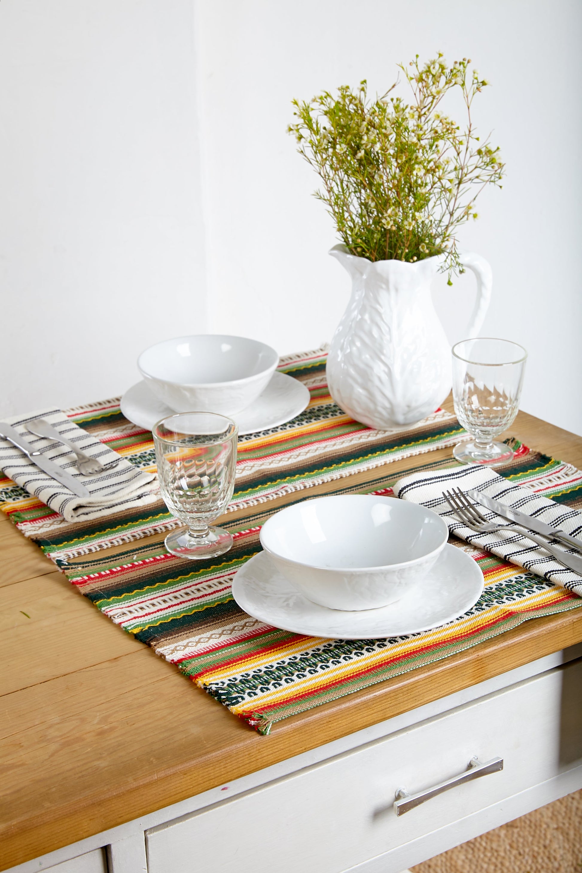 Mantel de mesa multicolor en rayas, hecho de algodón, con platos blancos y jarra de cerámica blanca.