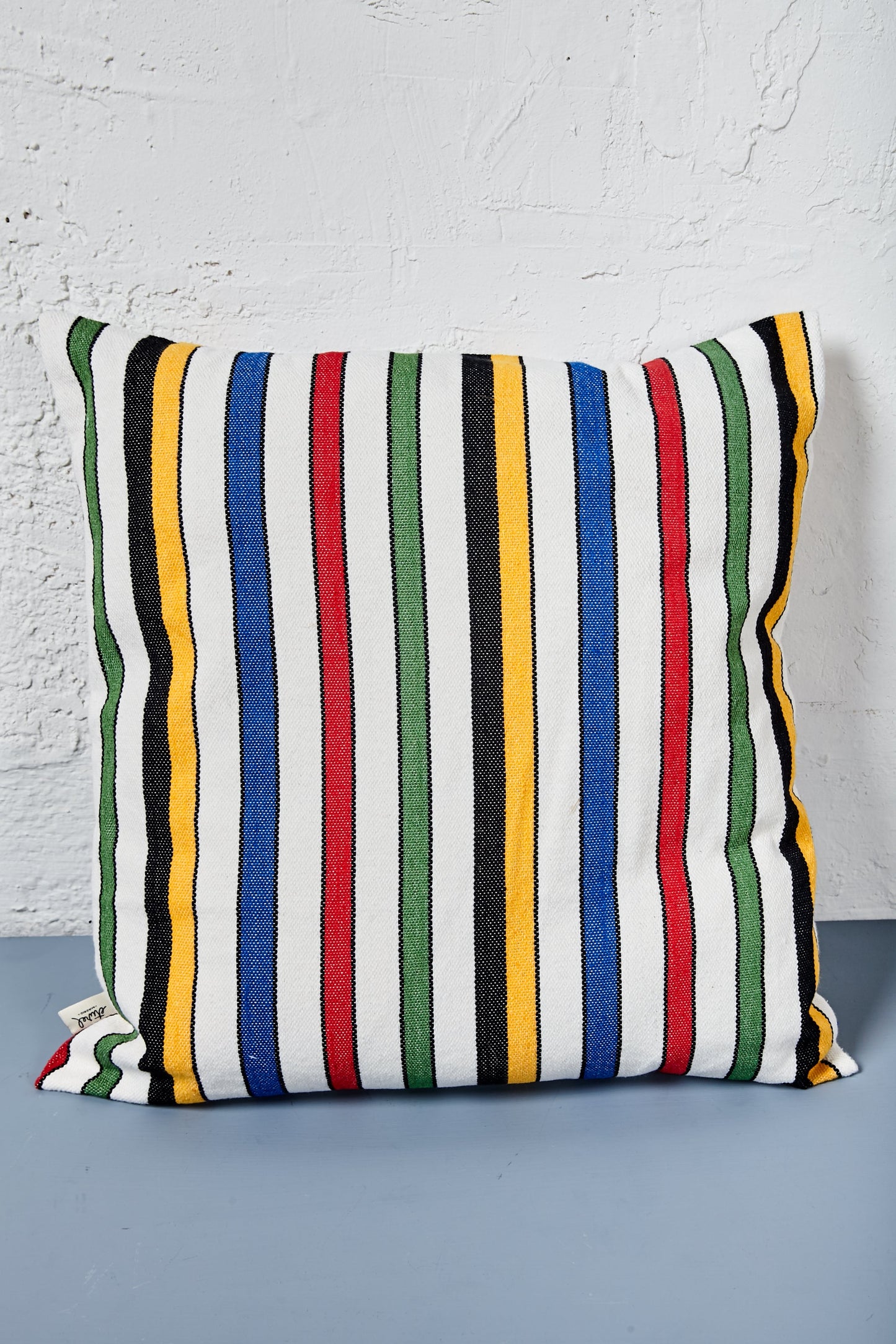 Cojín multicolor de rayas en tonos azul, verde, rojo, amarillo y negro, diseño moderno y tejido suave.