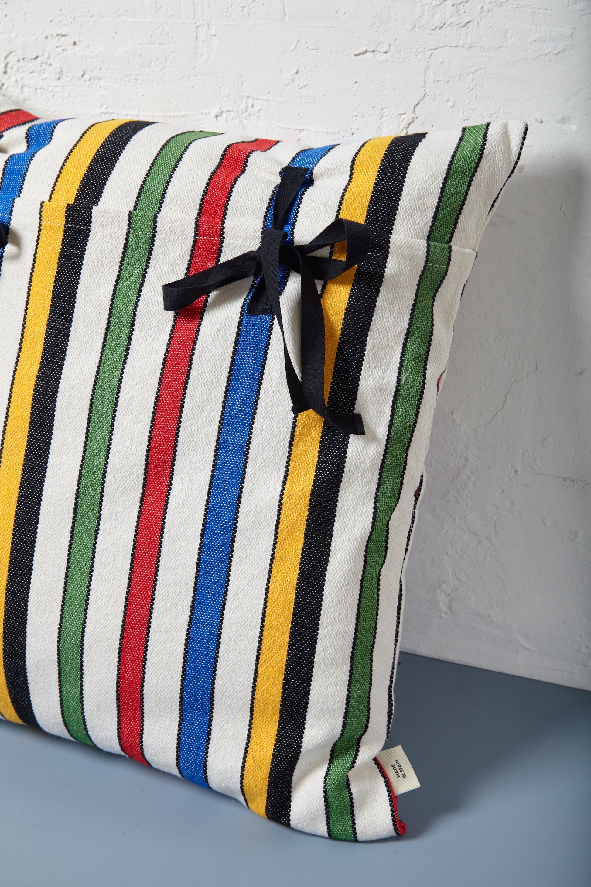 Cojín de rayas multicolores en algodón, con lazo negro, estilo moderno y alegre.