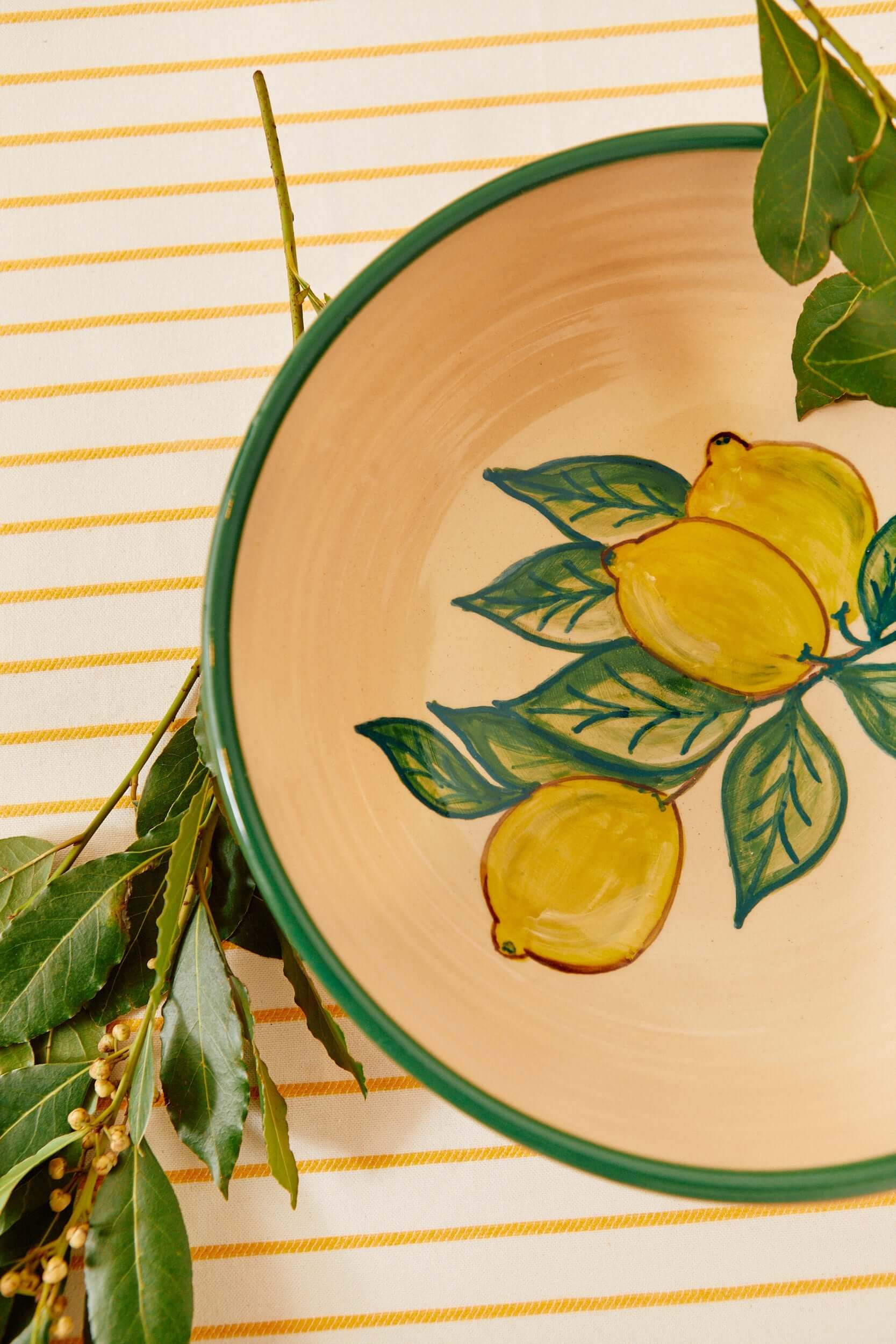 Detalle cercano de ensaladera cerámica limones sobre mantel amarillo con rama natural - bowl artesanal decorativo estilo mediterráneo