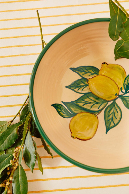 Detalle cercano de ensaladera cerámica limones sobre mantel amarillo con rama natural - bowl artesanal decorativo estilo mediterráneo