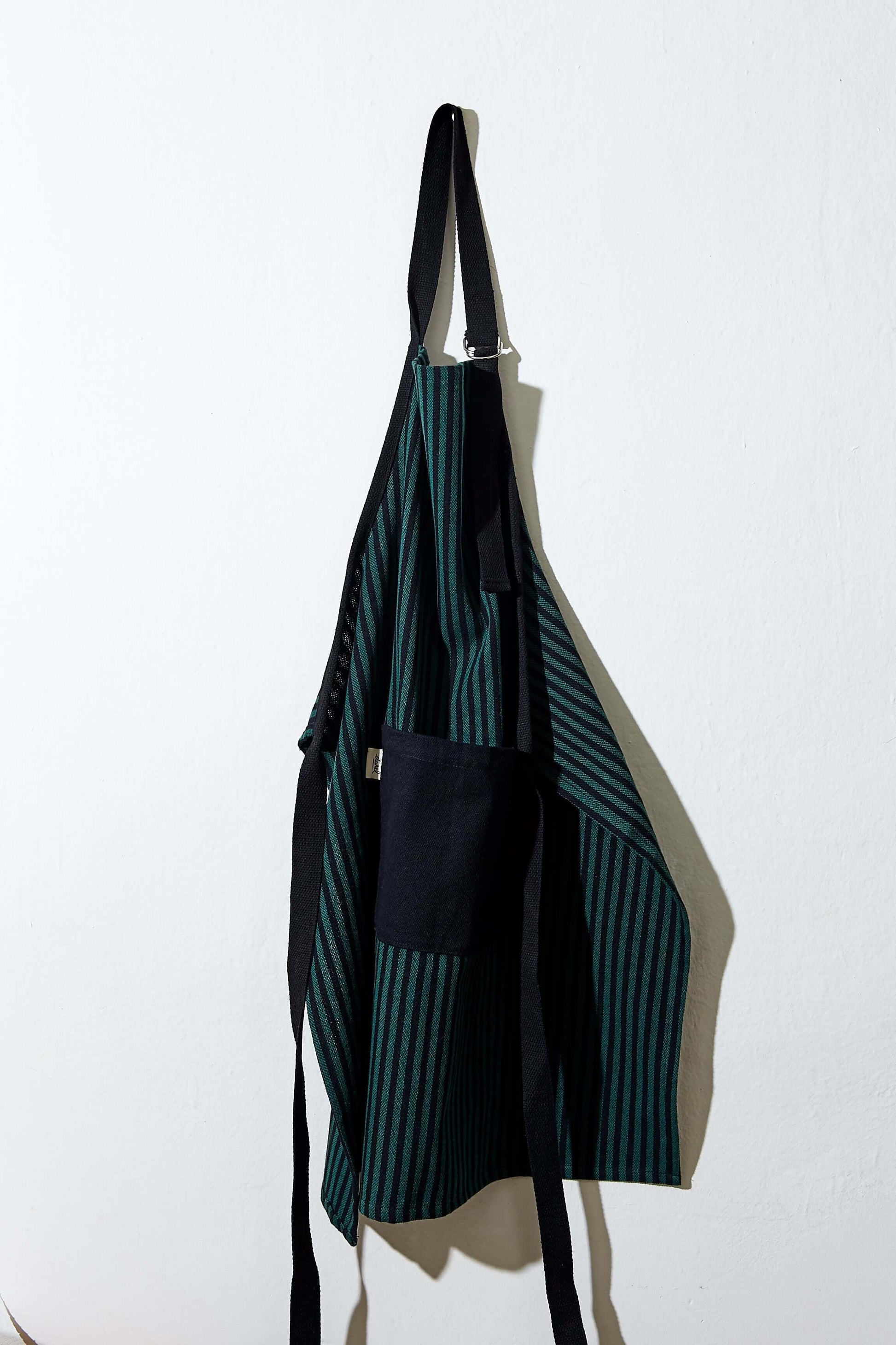 Delantal loneta estribera verde con rayas negras colgado mostrando bolsillo frontal